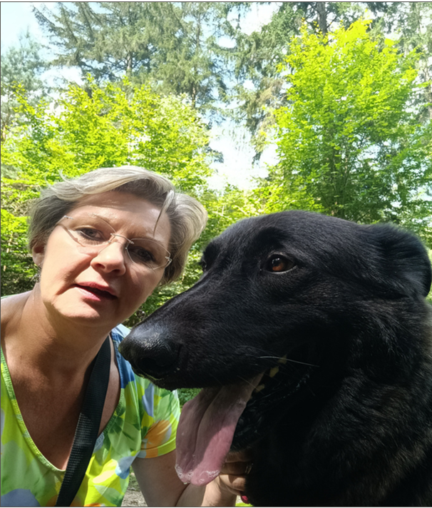 Die Künstlerin Manuela Schenk lächelnd zusammen mit ihrem Hund Balou im Gras